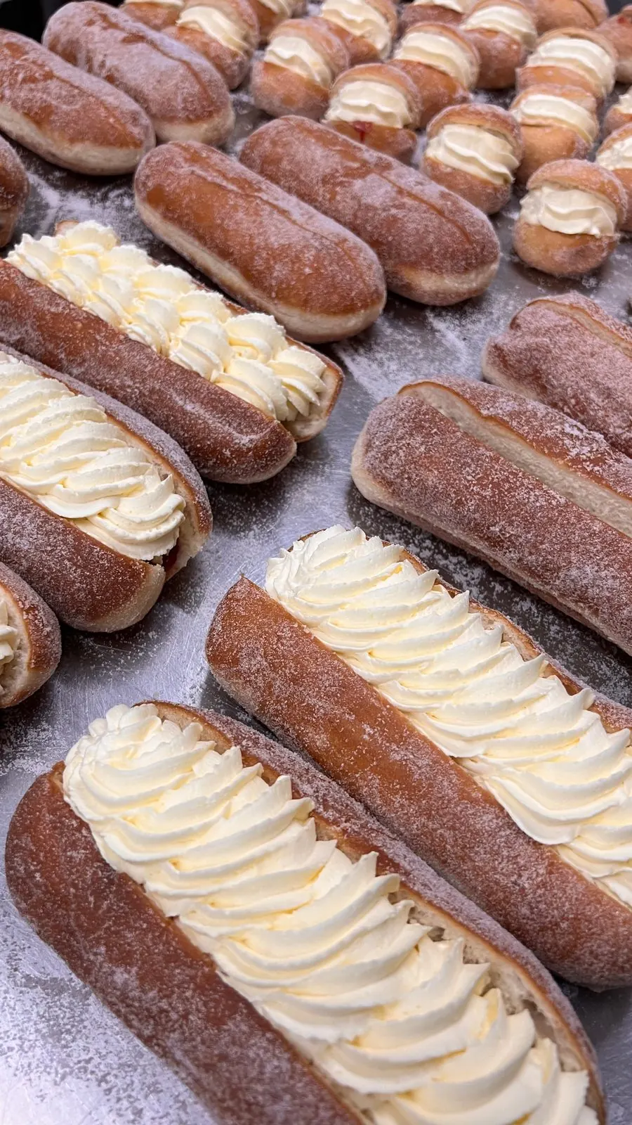 Trays of cream filled finger buns dusted with sugar.