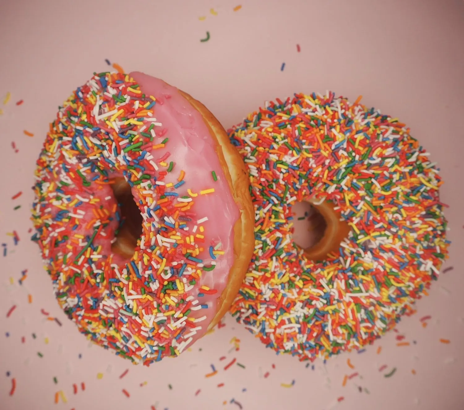 Two donuts covered in coloured sprinkles.
